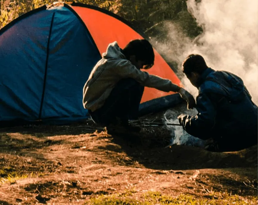 Two people sitting together beside a tent at dusk